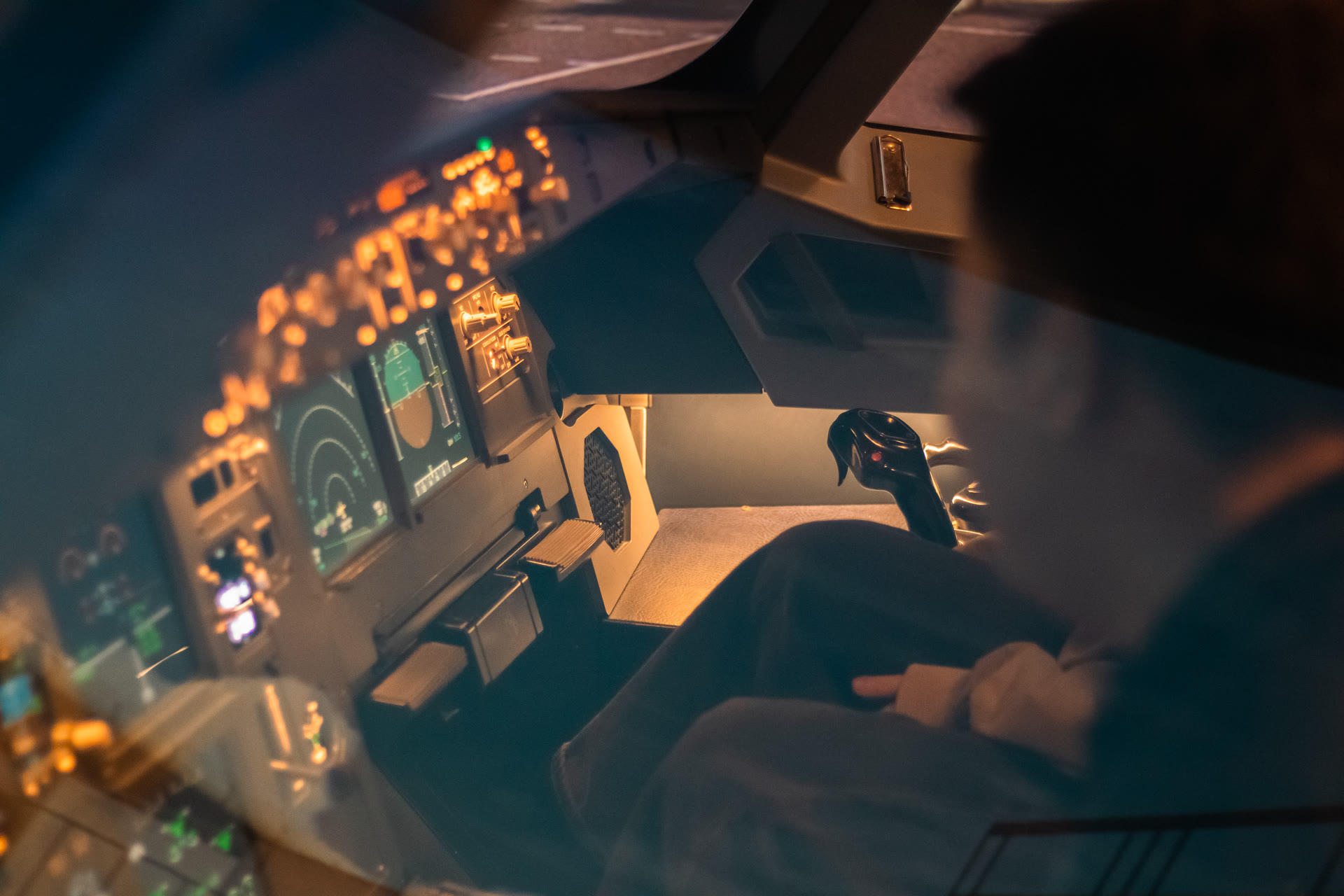 A pilot at the sidestick of the Airbus A320 simulator flight deck, cockpit displays glowing in a dim cabin